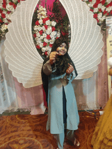 a woman in a hijab stands in front of a display of flowers and a sign that says ' welcome ' on it