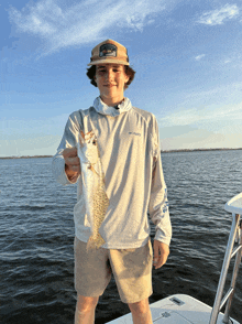 a boy wearing a columbia shirt holds a small fish