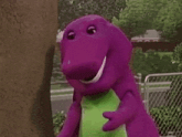 a purple dinosaur is standing next to a tree and laughing .