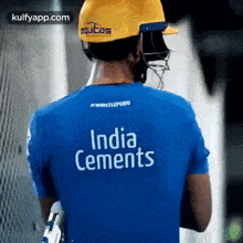 a man wearing a helmet and a blue shirt that says india cements is standing in front of a fence .