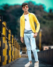 a young man wearing a yellow jacket and sunglasses is standing on a bridge .