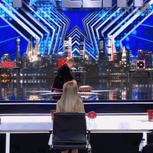 a woman sits in a chair in front of a stage with a city in the background and a sign that says ' america '