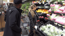 a man and a woman are looking at vegetables in a grocery store with a sign that says fresh watermelon