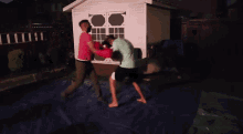 a man in a green shirt and a man in a pink shirt are boxing in front of a white shed