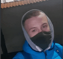 a man wearing a blue jacket and a black mask on his face is taking a selfie .