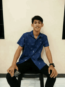 a young man in a blue shirt sits on a chair holding a cell phone