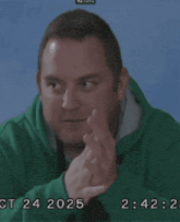 a man in a green hoodie is covering his face with his hands and the time is 2:42
