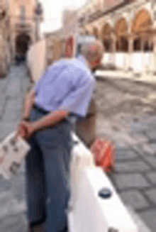 a man in a blue shirt is leaning on a white barrier on a sidewalk .