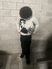 a person with curly hair wearing a white sweatshirt with a black r on it