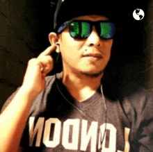 a man wearing sunglasses and ear buds is covering his ears with his finger .