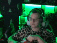 a man wearing headphones and glasses is sitting in a chair in a dark room with green lights .