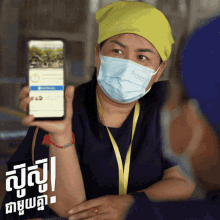 a woman wearing a mask holds up a cell phone