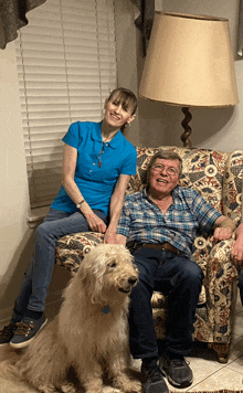 a woman in a blue shirt sits on a chair next to a man and a dog