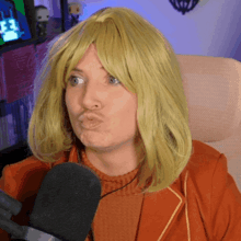 a woman wearing a yellow wig is sitting in front of a microphone and making a face