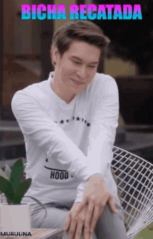 a man wearing a white shirt with the word hood on it is sitting in a chair