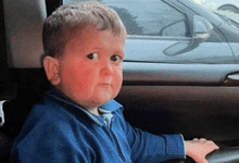 a young boy in a blue sweater is sitting in a car