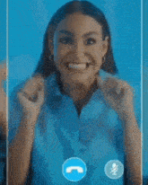 a woman in a blue shirt is talking on a video call with her hands together .