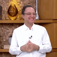 a man wearing glasses and a white shirt is smiling in front of a shelf with vases on it .