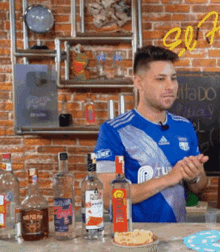 a man wearing a blue shirt with the letter p on it stands in front of a table with bottles of alcohol on it