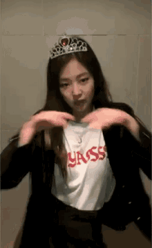 a woman wearing a tiara and a t-shirt making a heart shape with her hands .