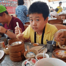 a boy in a yellow shirt is sitting at a table with other people eating food