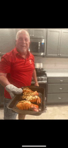 a man in a red shirt is holding a pan of lobsters in a kitchen .