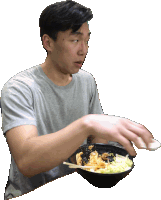 a man in a grey shirt is holding a bowl of food with chopsticks