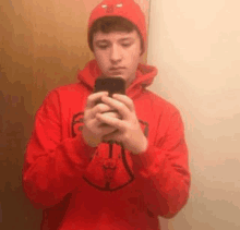 a young man in a red hoodie is taking a selfie with his phone .