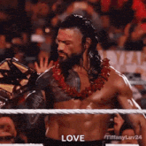 roman reigns is wearing a lei and holding a wrestling championship belt in a wrestling ring .