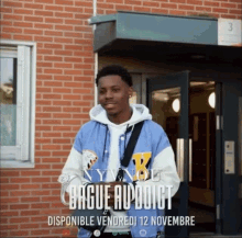 a man in a blue jacket stands in front of a brick building with a sign that says bague addict