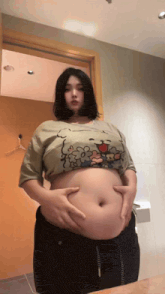 a woman in a crop top is holding her belly in front of a mirror