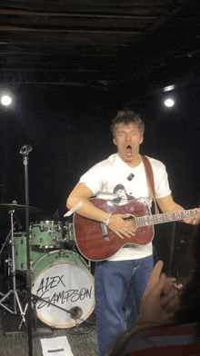 a man is playing a guitar in front of a drum that says alex simpson