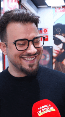 a man wearing glasses is smiling in front of a red fabrica de culos microphone