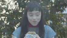 a young girl is eating a hamburger outside in front of a tree .