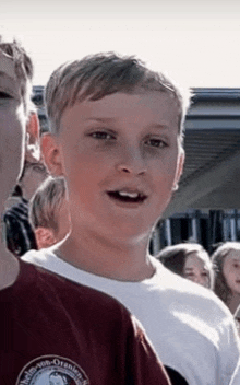 a young boy wearing a white shirt and a red shirt is standing in a crowd .