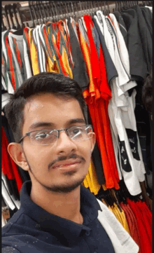 a young man wearing glasses takes a selfie in front of a rack of clothing