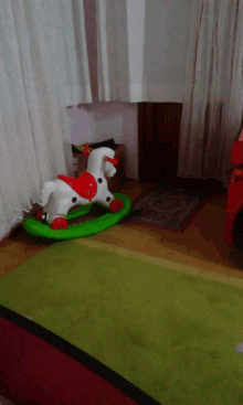 a rocking horse with red wheels sits on a green mat