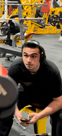 a man wearing headphones sits in a gym looking at his phone