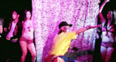 a man in a yellow shirt is dancing with a group of women