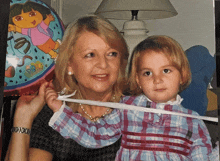 a woman holding a little girl with a dora balloon in the background