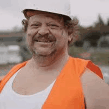 a man wearing a hard hat and an orange vest is smiling and looking at the camera .