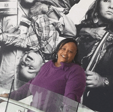 a woman in a purple sweater is smiling in front of a black and white photo