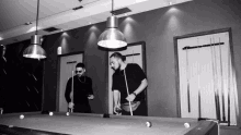 two men are playing pool on a pool table in a black and white photo