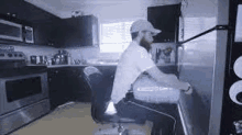 a man with a beard is sitting in a chair in a kitchen next to a refrigerator .