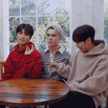 three young men are sitting at a table and one of them is wearing a striped shirt with the word happiness on it