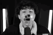 a black and white photo of a young man singing into a microphone with circles coming out of his mouth .