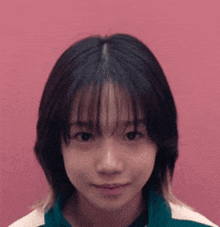 a young woman with short hair is standing in front of a pink background and looking at the camera .