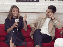 a man and a woman are sitting on a red couch with a sign that says international in the background