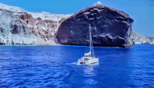 a sailboat is floating in the ocean near a large rock formation