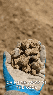 a person wearing a blue glove is holding a pile of rocks with the caption chipping away at the rock